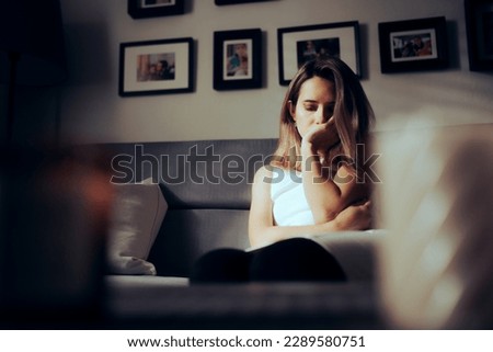 
Sad Depressed Woman Alone at Home Sitting on a Sofa. Unhappy lady feeling lonely and anxious in pain
