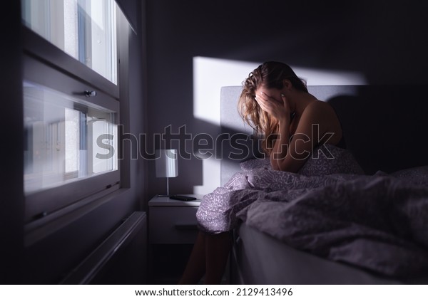 Sad depressed woman in bed. Lonely person with\
stress, insomnia and trouble sleeping. Anxiety, sorrow, solitude,\
grief or panic. Restless tired and desperate girl crying with\
emotion.