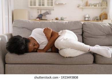 Sad Depressed Young African Woman With Crossed Arms Lying On Couch At Home Crying, Feeling Loneliness, Suffering From Breakup. Upset Black Girl Has Mental Problems, Can Not Forget Her Boyfriend. 