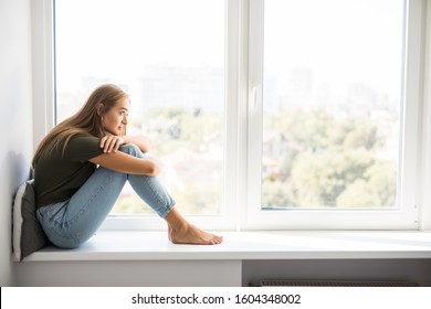 Sad depressed young teenage woman having social problems sitting on windowsill