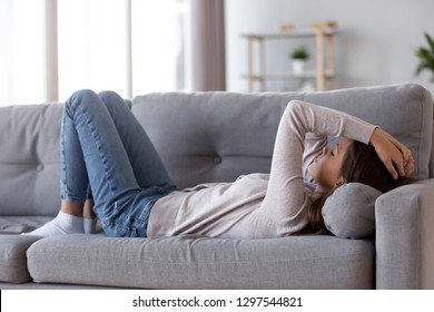 Sad depressed young woman lying on couch at home feeling headache fatigue loneliness, upset tired sick ill teen girl suffer from migraine anxiety, drowsy somnolent teenager rest on sofa after stress