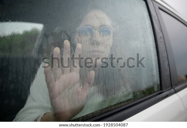 Sad and\
desolate woman places her hand on the car glass while it is\
raining. Concept of depression in the\
car.