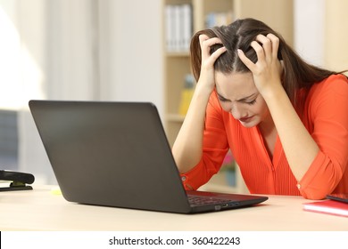 Sad and desperate freelancer female working on line with a laptop with her hands on the head sitting in an office desk or home interior