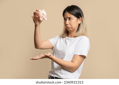 Sad and disappointed beautiful Asian woman holding a piggy bank with no money left.