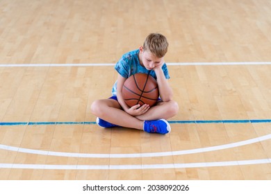 Sad disappointed boy sitting on basketball ball in a physical education lesson. Safe back to school during pandemic concept