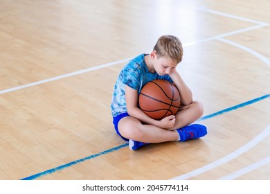 Sad disappointed boy sitting on basketball ball in a physical education lesson. Safe back to school during pandemic concept - Powered by Shutterstock