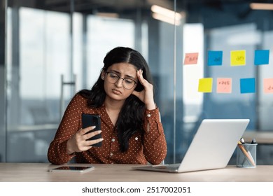 Sad disappointed business woman holding phone in hands, office worker received message with bad news online, latin american woman unhappy with business result inside building. - Powered by Shutterstock