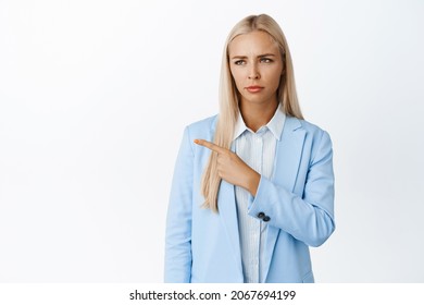 Sad And Disappointed Businesswoman, Pointing And Looking Left With Annoyed, Fed Up Face Expression, Standing In Suit Over White Background