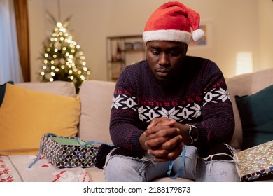 Sad disappointed man spends alone Christmas Eve, Day, wearing a Santa hat on head, unwrapping the wrong present and he has bad mood, crying - Shutterstock ID 2188179873