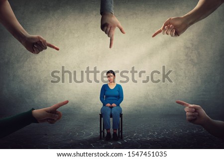 Sad and disappointed woman sitting on a chair looking indisposed being under pressure, feels discomfort as a lot of fingers pointing to her blaming as guilty. Human depression, social victim concept.