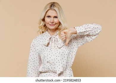 Sad Displeased Irritated Dissatisfied Elderly Gray-haired Blonde Woman Lady 40s Years Old Wears Pink Dress Showing Thumb Down Dislike Gesture Isolated On Plain Pastel Beige Background Studio Portrait