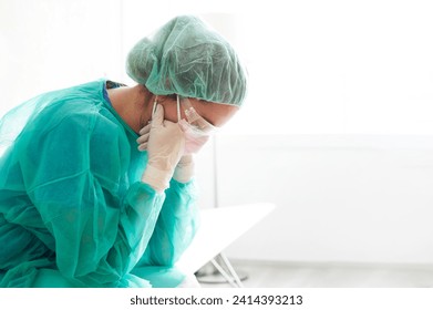 Sad doctor wearing protective workwear sitting against window in hospital - Powered by Shutterstock