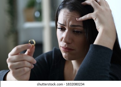 Sad doubtful wife looks at wedding ring thinking in divorce alone at home in the night