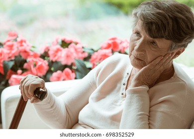 Sad elder lady sitting on the sofa and worrying about her health