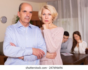 Sad Elderly Couple On A Background Of Adult Children With Documents