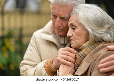 Sad Elderly Couple Standing Embracing Outdoors