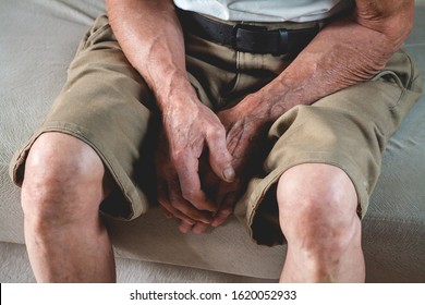 A Sad Elderly Senior Sits On A Sofa. Hands And Feet Closeup