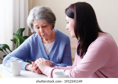 Sad elderly woman is comforted by a young woman and holds her hand - Girl volunteer supports a pensioner - The concept of family relationships and mental health