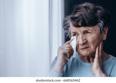 Sad elderly woman with teary eyes looking through the window