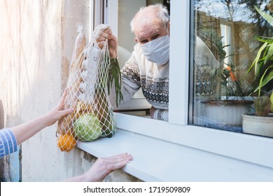 A Sad Elderly Wrinkled Woman Is Looking Through The Window In The Protective Mask Of Her House. Self-isolation Of The Elderly Coronavirus Covid-19. Quarantine And Isolation To Keep Old People Healthy