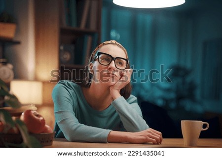 Sad exhausted woman sitting at the desk at home and having a break, she is thinking and looking away