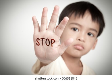 sad face of asian kid and hand raise stop written on his hand.