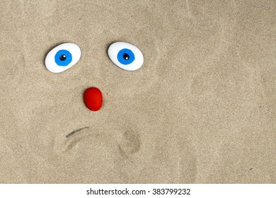 A Sad Face Drawn In The Sand With A Red Nose And Blue Eyes