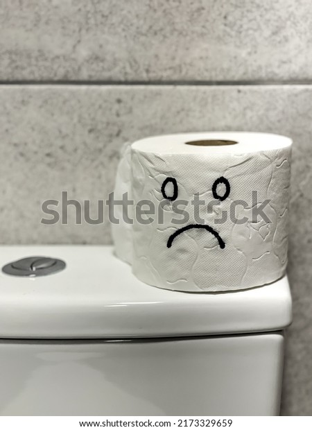 sad face painted on toilet paper roll.\
concept of constipation at home in\
bathroom