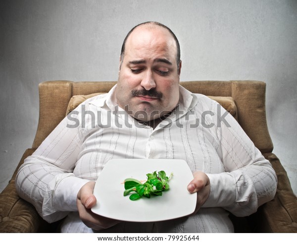 Sad fat man looking at a dish with some salad