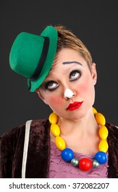 Sad Female Clown In A Green Hat On A Gray Background
