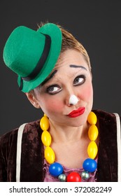 Sad Female Clown In A Green Hat On A Gray Background
