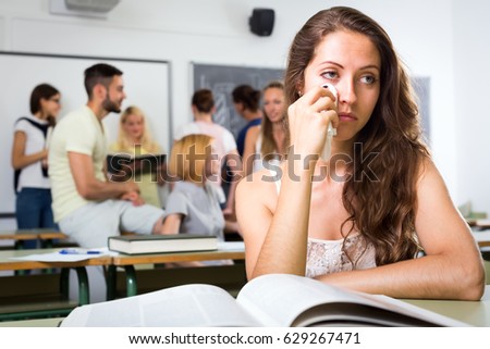 Sad female highschool student sitting at her desk in classroom and wiping tears