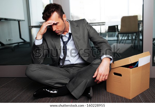 Sad fired businessman sitting outside meeting\
room after being dismissed