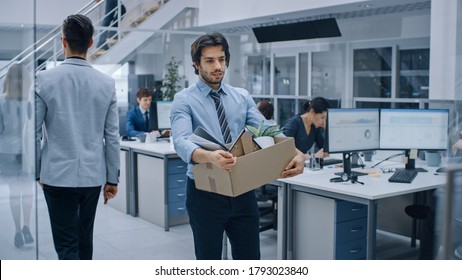 Sad Fired / Let Go Office Worker Packs His Belongings Into Cardboard Box And Leaves Office. Workforce Reduction, Downsizing, Reorganization, Restructuring, Outsourcing. Shot With Dark Ambient