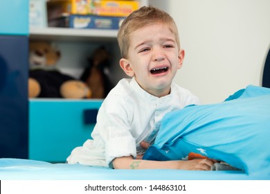 A Sad Five Year Old Child Sitting Next To His Bed With Holding A Pillow And Crying