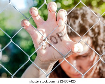 Sad and frightened woman leaning behind a fence with the word stop written on her hand.Concept of feminism, demand for equality and an end to violence against women.Concept of stop war.Selective focus