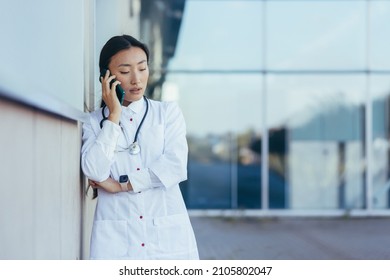 Sad And Frustrated Female Doctor Talking On The Phone Near The Clinic, Asian Depressed And Tired After Work