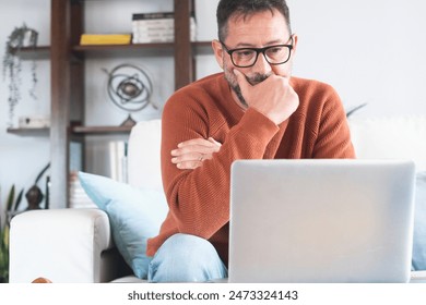 Sad and frustrated man feeling tired and worried about a problem sitting on sofa at home with laptop, stressed 50 year old male having problems reading bad news online, email notification about debt  - Powered by Shutterstock