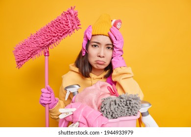 Sad Frustrated Young Asian Woman Suffers Headache After Doing Much Work About House Hates Laundry Holds Mop To Clean Walls Of Room Isolated Over Yellow Background Expresses Negative Emotions