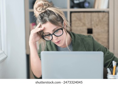 Sad and frustrated young woman feeling tired and worried about a problem sitting at desk with laptop, stressed and in pain female having problems reading bad news online, email notification about debt - Powered by Shutterstock