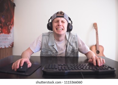 Sad Gamer Sits At Home Behind The Computer And Cries Of Defeat In The Video Game. Portrait Of A Funny Sad Teen Who Lost In A Computer Game. Gamer Concept