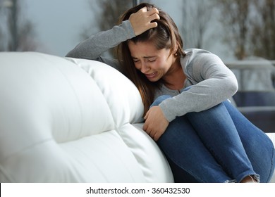 Sad girl crying desperately alone sitting on a couch at home in a dark winter day - Powered by Shutterstock