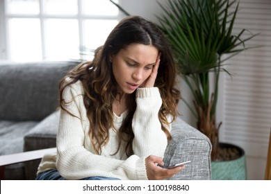 Sad girl feeling upset reading bad news in mobile message on smartphone at home, depressed frustrated young woman holds phone scared of threatening suffering from cyberbullying being bullied via cell