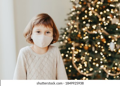 Sad Girl Meets Christmas In The Covid-19 Pandemic. Child In A Protective Medical Mask. Quarantine Isolation Social Distance. New Year Holidays 2021. Kid In Face Cover