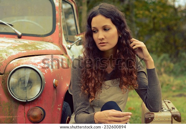 Sad girl sits in an old retro car with suitcase\
with vintage effect