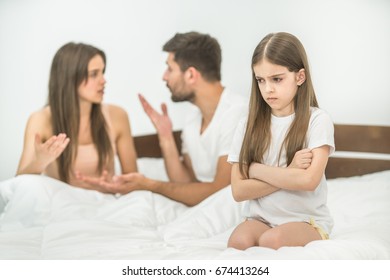 The sad girl sitting near the gesture parents on the bed