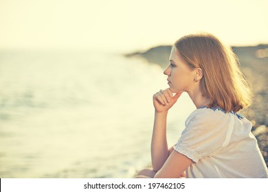 sad girl sitting on the coast on beach and looks into the distance at sea