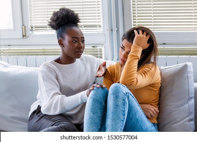 Sad girl and supporting friends trying to solve a problem. Two sad diverse women talking at home. Female friends supporting each other. Problems, friendship and care concept