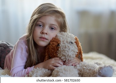 Sad girl with a toy dog on the bed