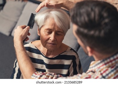 sad grandmother with closed eyes getting her coiffure fixed by her middle-aged millennial son. High quality photo